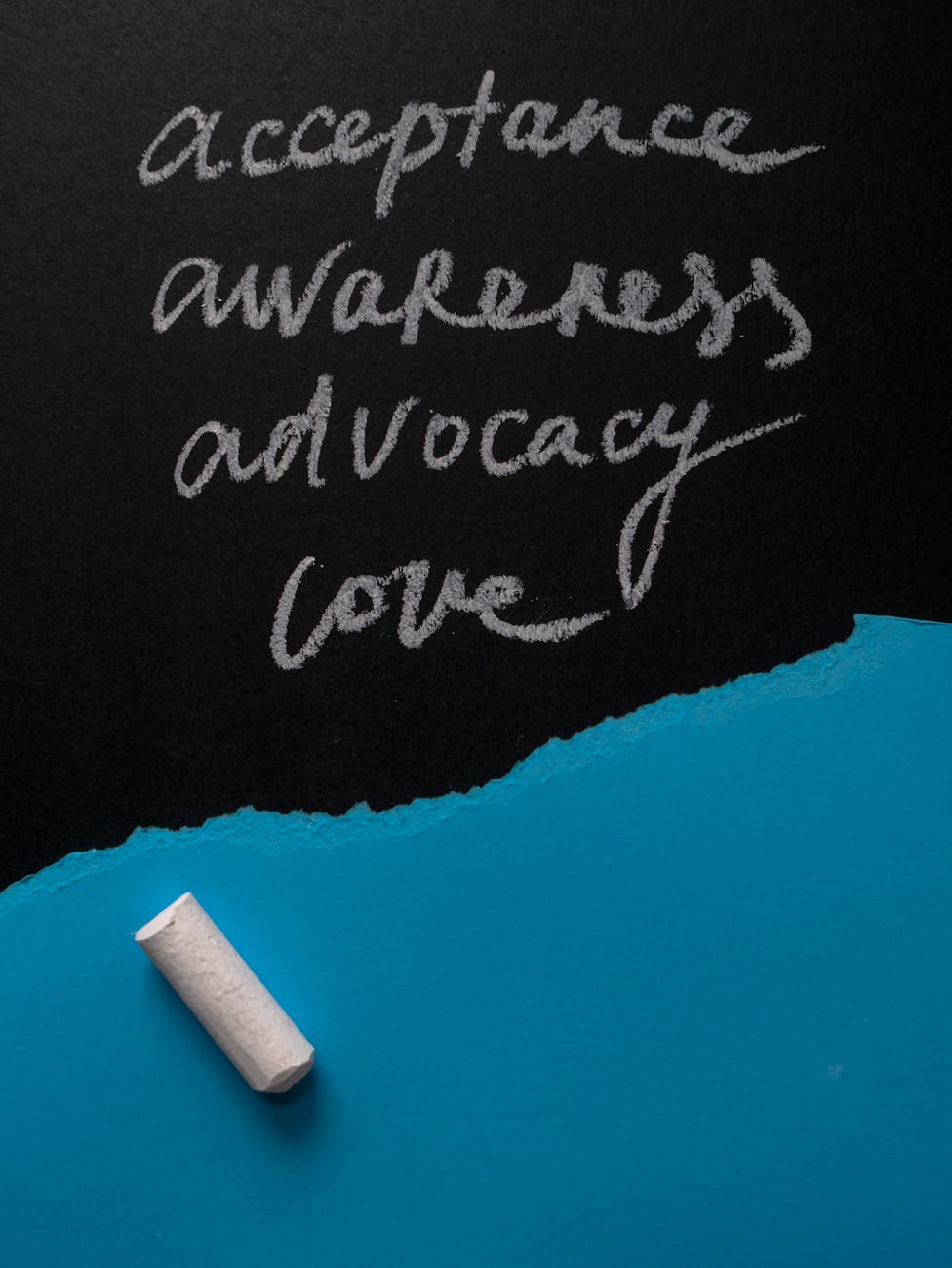 Handwritten chalk words promoting acceptance and advocacy on a blackboard with a piece of chalk.